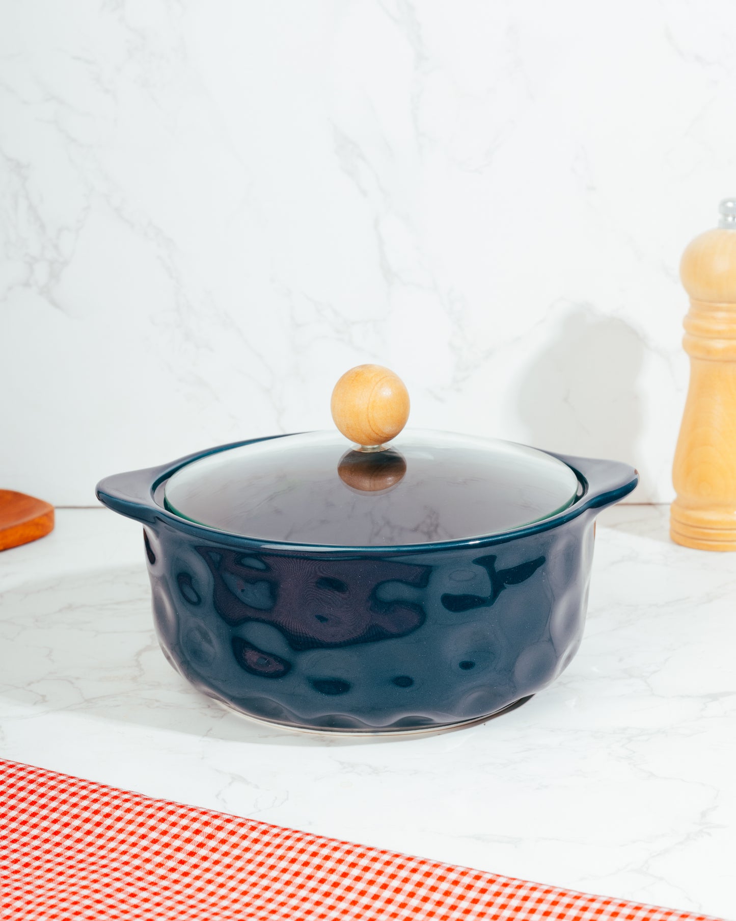 A blue ceramic pot with a lid, featuring a wooden handle knob, placed on a kitchen countertop.