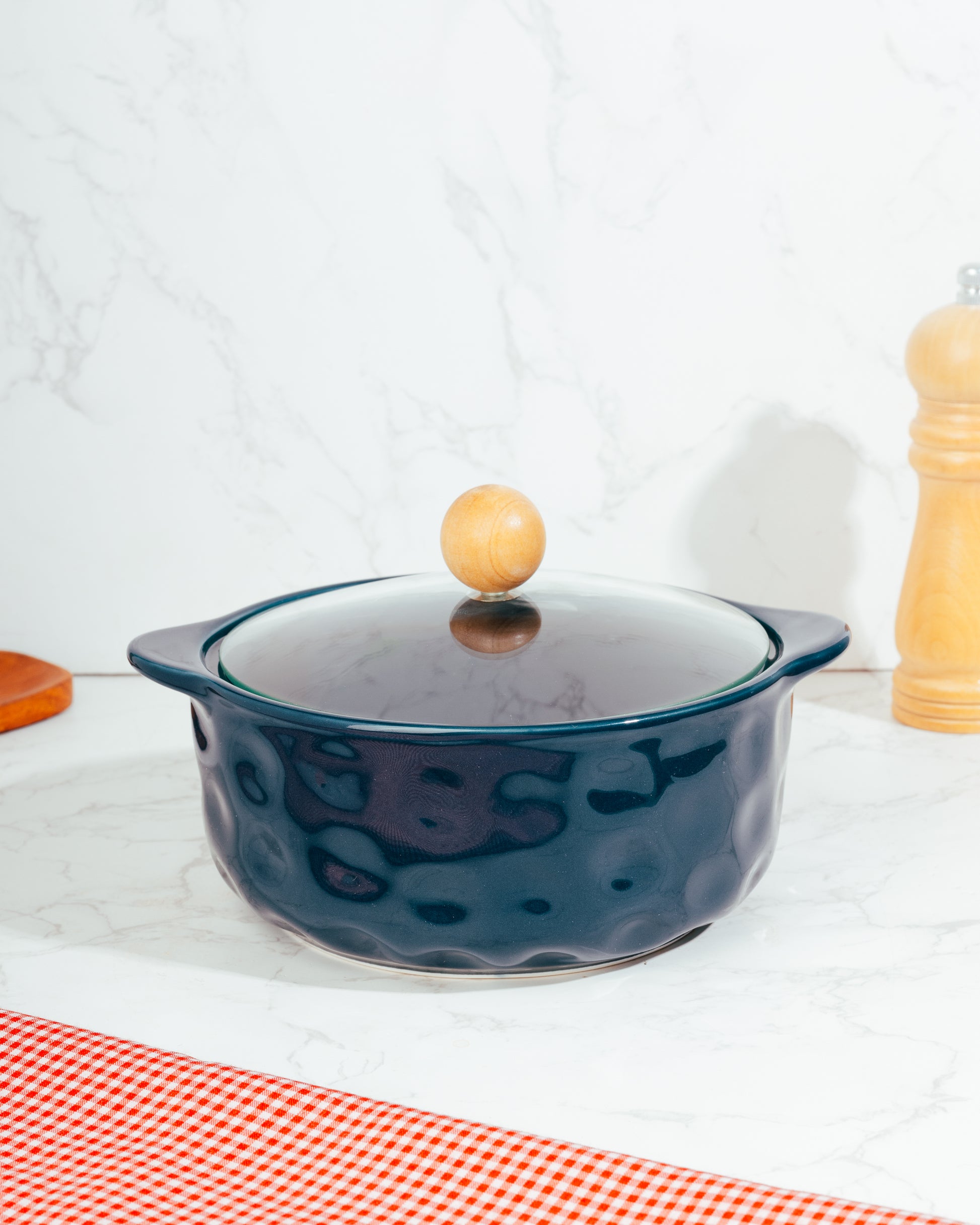 A blue ceramic pot with a lid, featuring a wooden handle knob, placed on a kitchen countertop.