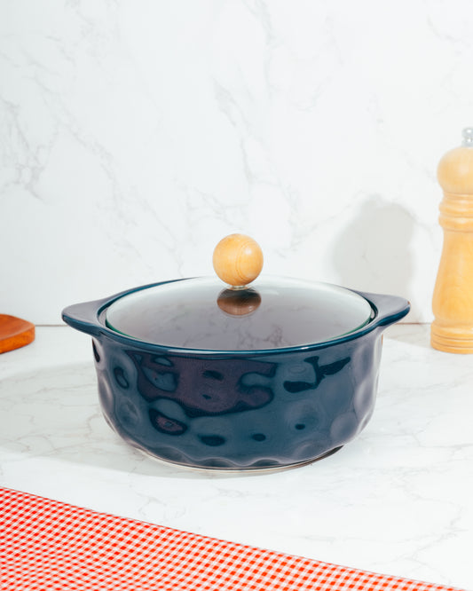 A blue ceramic pot with a lid, featuring a wooden handle knob, placed on a kitchen countertop.
